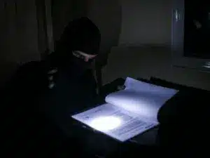 inbreker die document in het donker doorneemt met zaklamp